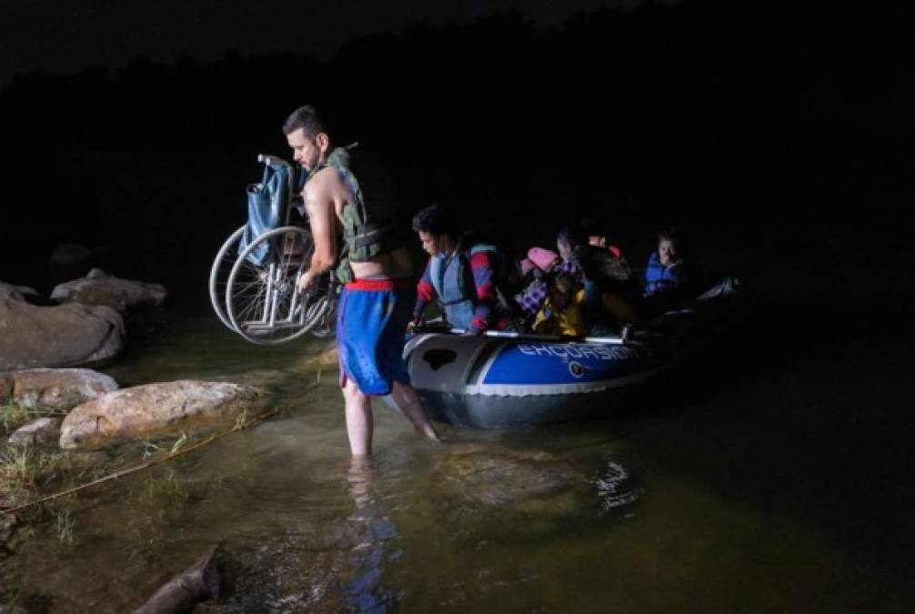 Un hombre carga la silla de ruedas a la orilla del Río Grande para la inmigrante hondureña de 93 años Trinidad Tabora.