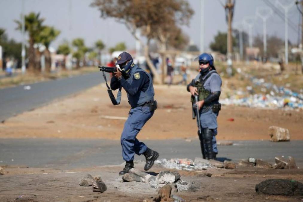 A member of the South African Police Services (SAPS) aim at looters following sporadic looting and vandalism outside the Lotsoho Mall in Katlehong township, East of Johannesburg, on July 12, 2021. Several shops are damaged and cars burnt in Johannesburg, following a night of violence. Police are on the scene trying to control further protests. It is unclear if this is linked to sporadic protests following the incarceration of former president Jacob Zuma. (Photo by Phill Magakoe / AFP)