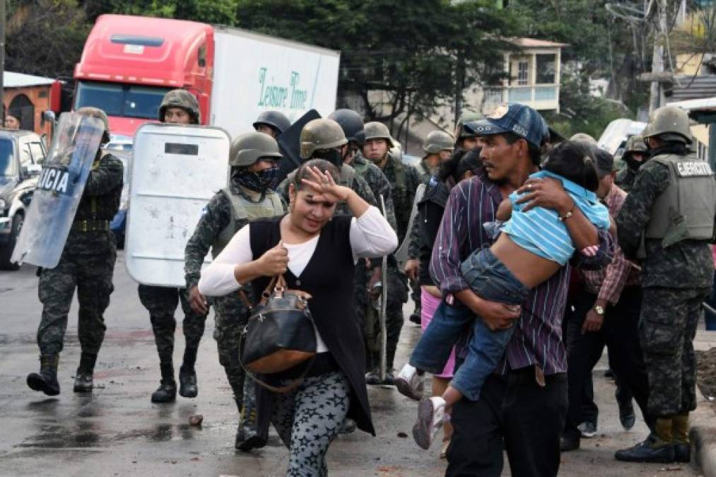 Residents get away from clashes between riot police and supporters of opposition candidate Salvador Nasralla, during protests in Tegucigalpa, on December 18, 2017.<br/>Honduran President Juan Orlando Hernandez is declared the winner of a heavily disputed presidential election held three weeks ago, despite mounting protests and opposition claims of fraud. / AFP PHOTO / ORLANDO SIERRA