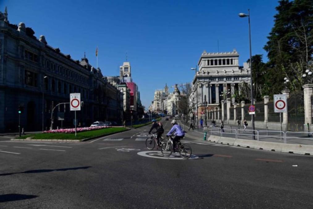 Los ciclistas pasan hoy por la Plaza de Cibeles mientras las avenidas permanecen vacías en Madrid después de que las autoridades regionales ordenaron que se cerraran todas las tiendas de la región desde hoy hasta el 26 de marzo, a excepción de las que venden alimentos, químicos y estaciones de servicio, para frenar el coronavirus.