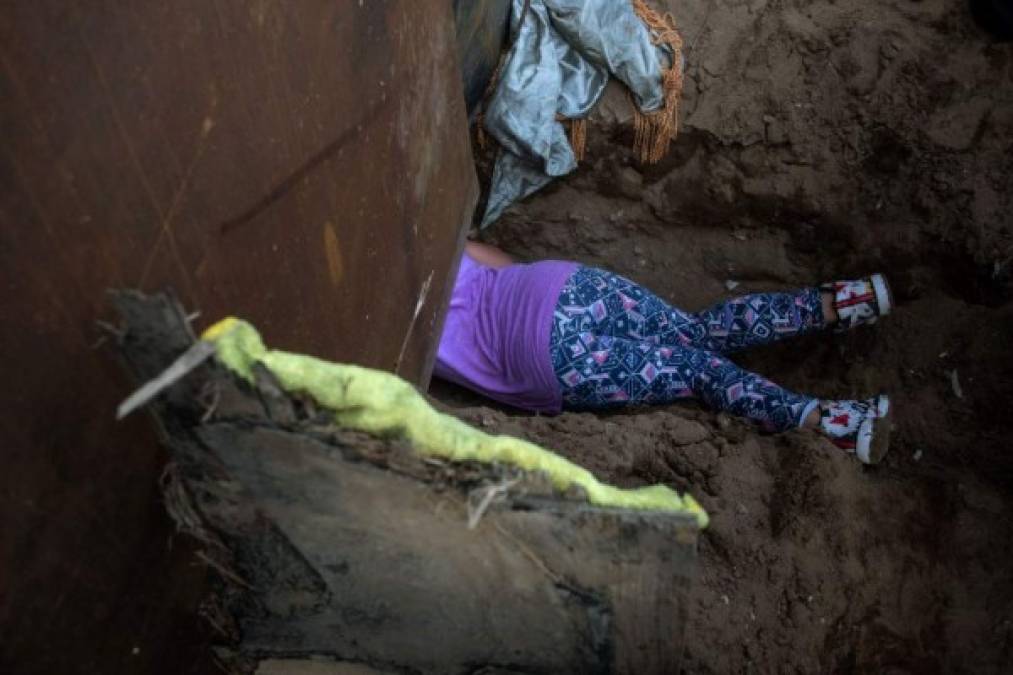 Honduran migrant Andrea Nicolle, 10, travelling in a caravan of Central American migrants hoping to get to the United States, crosses through a hole on the ground under the metal barrier separating Mexico and the US to cross from Playas de Tijuana in Mexico into the US, on December 4, 2018. - Mexico's new Foreign Minister Marcelo Ebrard met with US Secretary of State Mike Pompeo for a 'friendly' meeting amid tensions over the migrant crisis at the border. Both countries are grappling with how to handle the thousands of Central American migrants who are camped at the common border -- in the short and long terms. (Photo by Guillermo Arias / AFP)