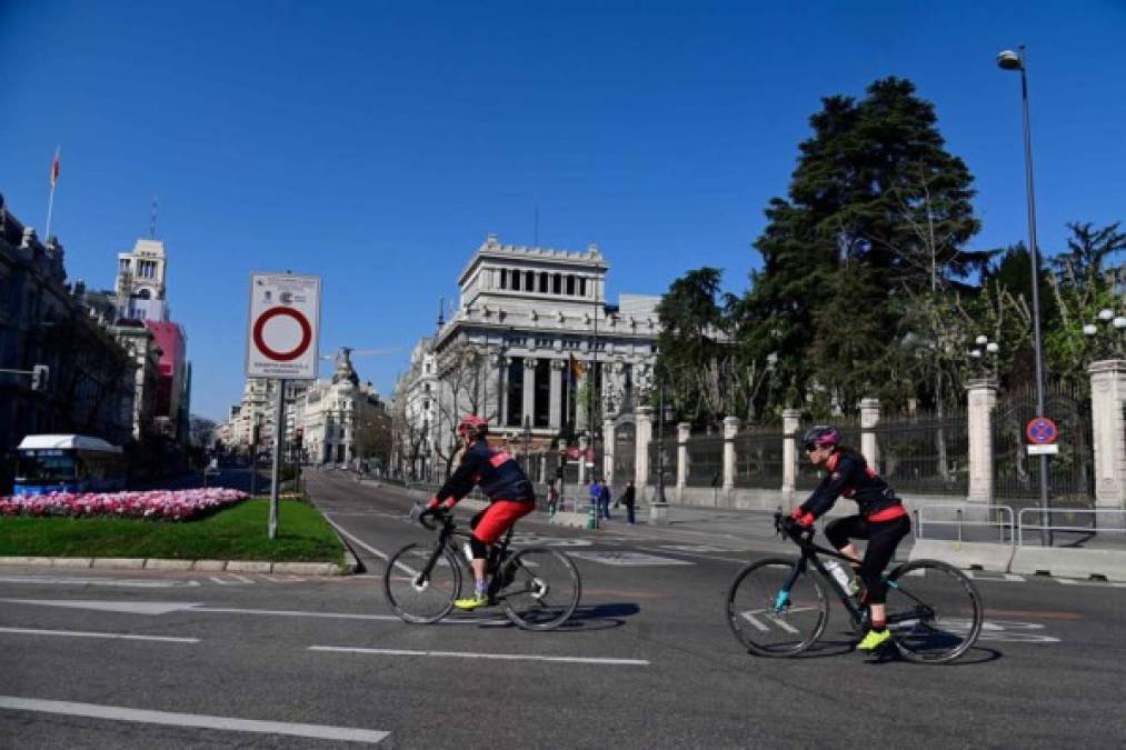 Los ciclistas pasando hoy por la Plaza de Cibeles mientras las avenidas permanecen vacías en Madrid, España.