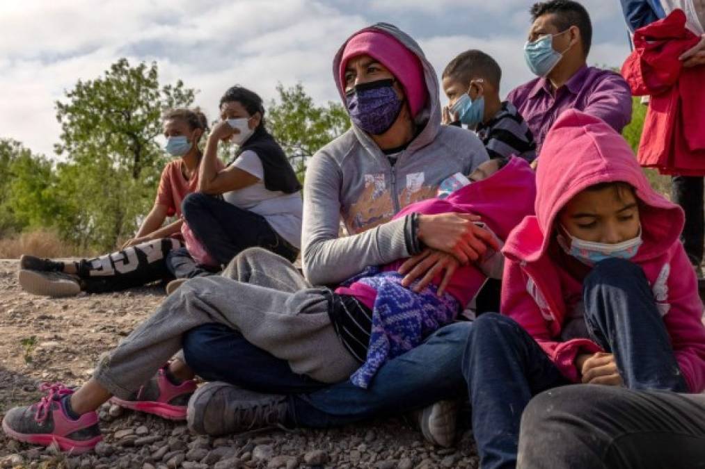 A group of migrants arriving from Mexico sit before state troopers and border patrol agents at a roadside after they were apprehended in a vehicle in the border city of Rio Grande, Texas, on March 27, 2021. (Photo by Ed JONES / AFP)