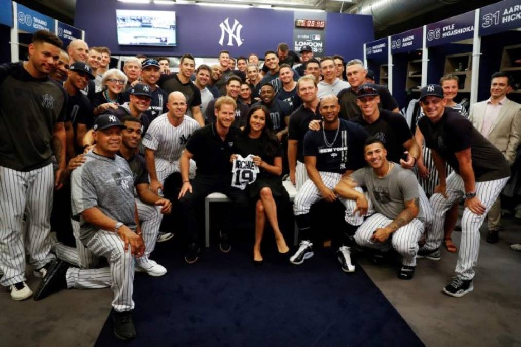 Meghan sostiene la camiseta de los Yankees de Archie mientras ella y el príncipe Harry se sientan con los Yankees de Nueva York previo al juego.<br/>El 19 estampado en la camisola es por el año del nacimiento del bebé.