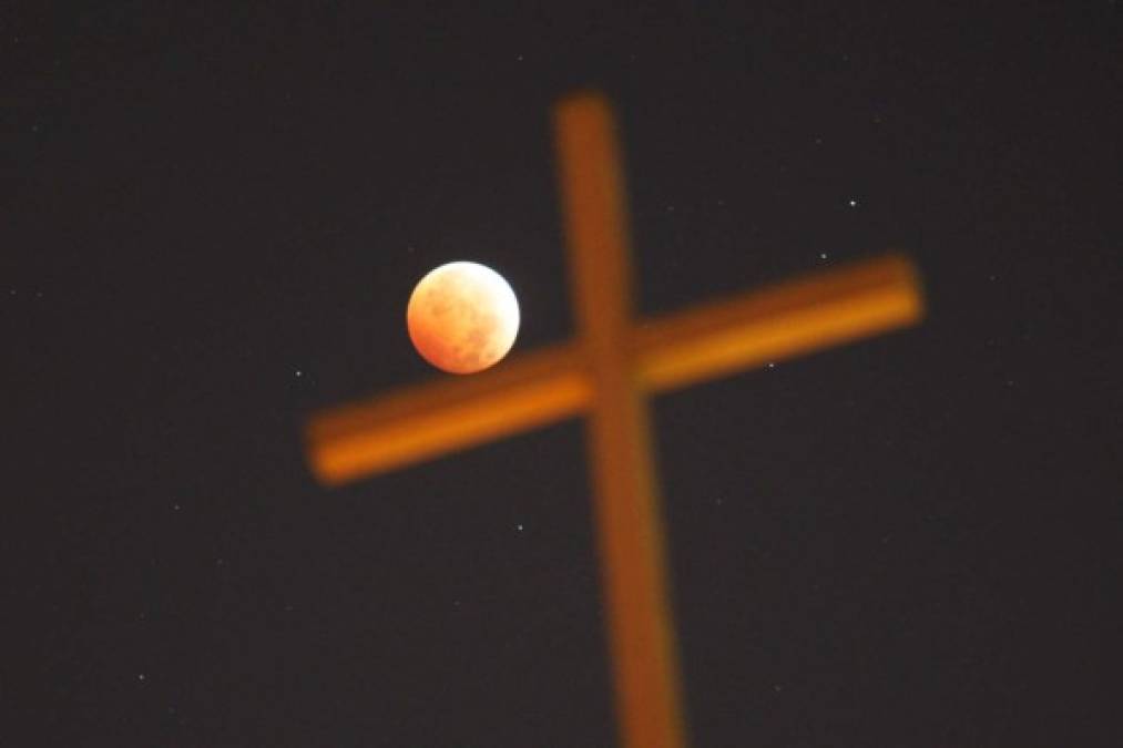 Una cruz religiosa es vista junto a la Luna que está iluminada por la luz solar reflejada por la Tierra durante un eclipse total lunar el 8 de octubre de 2014 en Los Angeles, California. AFP
