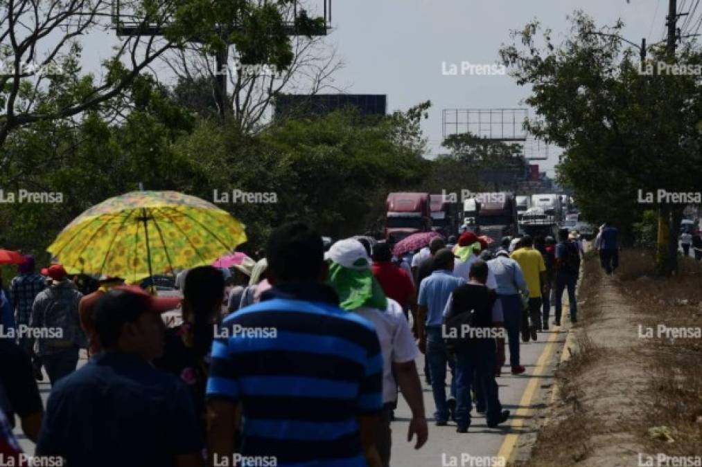 Mientras los manifestantes marchan por la carretera, el transporte de carga espera a lo lejos.