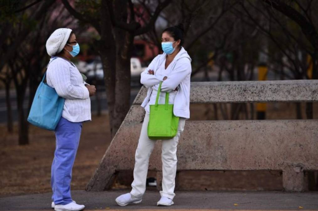 Workers of the health sector wear face masks as a preventive measure against the spread of the new coronavirus, COVID-19, as they wait at a bus stop in Tegucigalpa on March 16, 2020. - Quarantine, schools, shops and borders closed, gatherings banned, are the main measures being taken in many countries across the world to fight the spread of the novel coronavirus. (Photo by Orlando SIERRA / AFP)