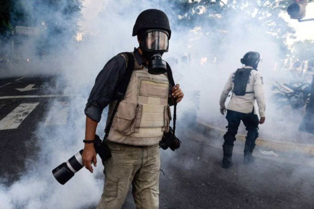 Wearing a flak jacket, protective helmet and gas mask, a photojournalist wades through a cloud of tear gas as opposition activists demonstrating against the government of Venezuelan President Nicolas Maduro clash with riot police in Caracas on June 26, 2017. <br/>A political and economic crisis in the oil-producing country has spawned often violent demonstrations by protesters demanding Maduro's resignation and new elections. The unrest has left 75 people dead since April 1. / AFP PHOTO / FEDERICO PARRA