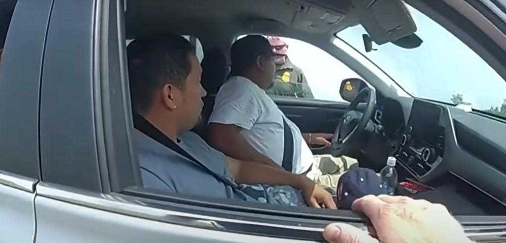 El policía se inclina en la ventana de Velásquez Larín para presentarse y decirle a García que lo están deteniendo por seguir muy de cerca a otro carro.