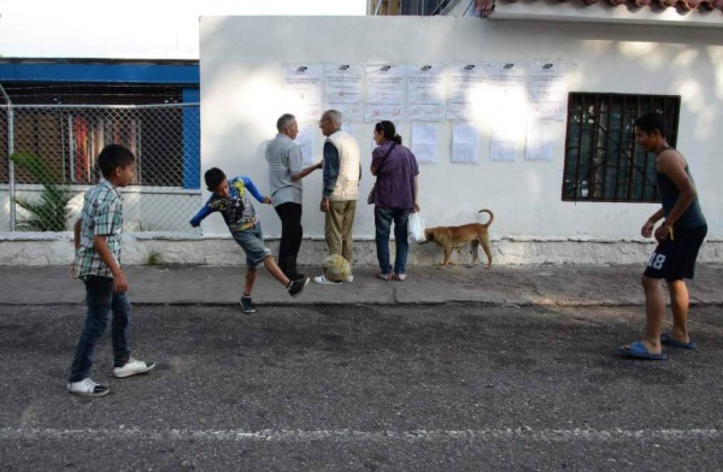 Jóvenes juegan fútbol mientras la gente revisa el registro electoral antes de emitir su voto en San Cristóbal, Venezuela. AFP<br/>