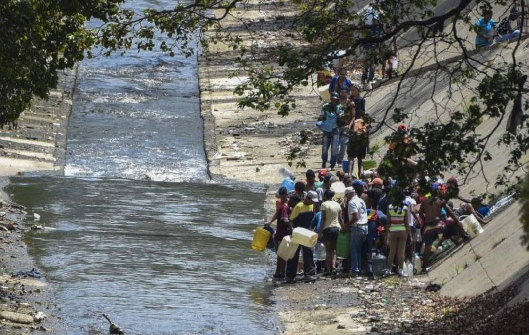 CORRECTION - People collect water from a broken pipe flowing into a sewage canal at the Guaire river in Caracas on March 11, 2019, as a massive power outage continues affecting some areas of the country. - Venezuela's opposition leader Juan Guaido will ask lawmakers on Monday to declare a 'state of alarm' over the country's devastating blackout in order to facilitate the delivery of international aid -- a chance to score points in his power struggle with President Nicolas Maduro. (Photo by JUAN BARRETO / AFP) / The erroneous mention[s] appearing in the metadata of this photo by JUAN BARRETO has been modified in AFP systems in the following manner: [collect water from a broken pipe flowing into a sewage canal at the Guaire river] instead of [collect water from a sewage canal at the river Guaire]. Please immediately remove the erroneous mention[s] from all your online services and delete it (them) from your servers. If you have been authorized by AFP to distribute it (them) to third parties, please ensure that the same actions are carried out by them. Failure to promptly comply with these instructions will entail liability on your part for any continued or post notification usage. Therefore we thank you very much for all your attention and prompt action. We are sorry for the inconvenience this notification may cause and remain at your disposal for any further information you may require.