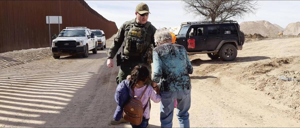 Shura Wallin lleva de la mano a una niña de 5 años, la cual viaja sola, para entregarla a un agente de la Patrulla Fronteriza en la frontera de Arizona.