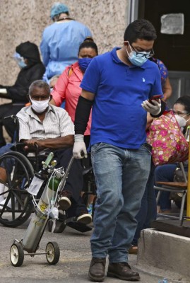 A man carries an oxygen tank for a relative allegedly infected with the new coronavirus at a field hospital set up in the yard of the School Hospital in Tegucigalpa, on July 1, 2020. - Honduras is overwhelmed by deaths caused by COVID-19 and the large number of people infected that are admitted every day in different hospitals across the country. (Photo by ORLANDO SIERRA / AFP)