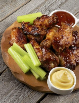 Spicy Chicken Legs and Wings Barbecue with Celery Sticks, Ketchup and Cheese Sauce on Wooden Plate closeup on Rustic Wooden background