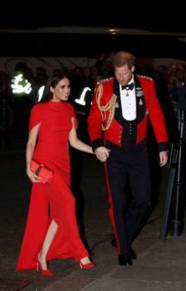 La duquesa de Sussex llevaba un vestido de capa Safiyaa rojo escarlata, que ella complementó con tacones Aquazzura, un bolso rojo de satén Manolo Blahnik y pendientes florales de Simone Rocha. Mientras Harry lucía su uniforme de gala como Capitán General de los Royal Marines. MIRA: <a href='https://www.laprensa.hn/fotogalerias/sociales/1361698-411/meghan-markle-primer-evento-oficial-tras-megxit' style='color:red;text-decoration:underline' target='_blank'>Meghan comienza a despedirse de la realeza en primer evento oficial tras anunciar Megxit</a>