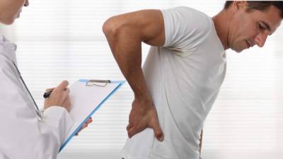 Female Doctor and male patient suffering from back pain during medical exam.