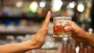 Una mano en señal de detente mientras otra mano le ofrece un vaso con alcohol