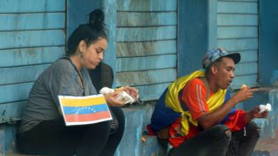 Dos venezolanos comen después de pedir en las calles de San Pedro Sula.
