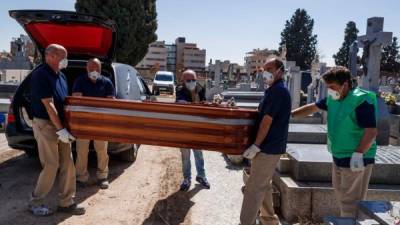 Mortuary employees wearing face masks carry the coffin of a COVID-19 coronavirus victim during a burial at the Fuencarral cemetery in Madrid on March 29, 2020. - Spain confirmed another 838 deaths in 24 hours from coronavirus , a new daily record bringing the total number of deaths to 6,528, according to health ministry figures. The number of confirmed cases in Spain has now reached 78,797 -- after the one-day increase of 9.1 percent -- as the country battles the world's second most deadly outbreak after Italy. (Photo by BALDESCA SAMPER / AFP)