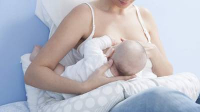 Young mother feeding breast. She is using a nursing pillow with the baby on side