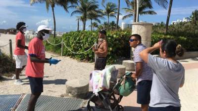 Unos jóvenes revisan las máscaras de unas personas a su llegada a la playa de Miami Beach, Florida.