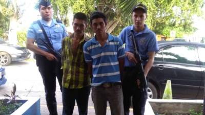 Dos personas detenidas, custodiadas por agentes de la Policía Nacional de Honduras.