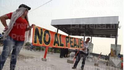 Una mujer y un hombre sostienen una pancarta en protesta por la construcción de las casetas de peaje.