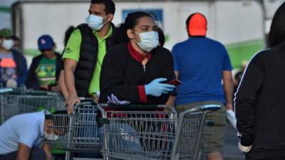 Las personas usan máscaras faciales y guantes mientras hacen cola para ingresar a un supermercado durante un descanso del toque de queda impuesto por el Gobierno. Foto AFP