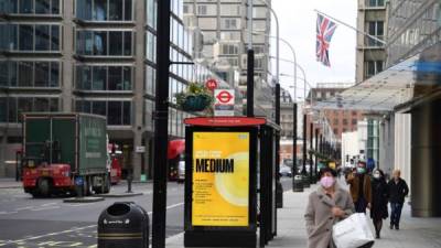 Un comprador pasa junto a un cartel que muestra el nivel de alerta de COVID-19 en un refugio de la parada de autobús a lo largo de Victoria Street, en el centro de Londres. Foto AFP