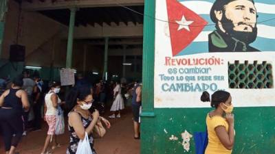Varias mujeres con tapabocas pasan junto a un cartel con la imagen de Fidel Castro.