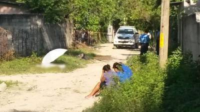 Dos mujeres y un hombre están sendados frente a un cadáver en la colonia Asentamientos Humanos de San Pedro Sula, zona norte de Honduras.