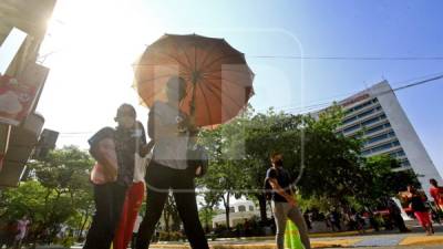 Con sombrillas, libros y hasta con las manos, los sampedranos buscan protegerse de los rayos del sol. Fotos: Moisés alenzuela y Yoseph Amaya.