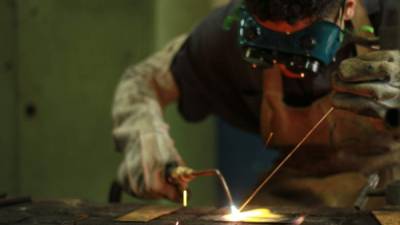 Estudiante de curso de construcciones metálicas soldando una pieza de metal.