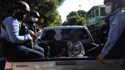 La pareja siendo custodiada por policías en la paila de un vehículo.