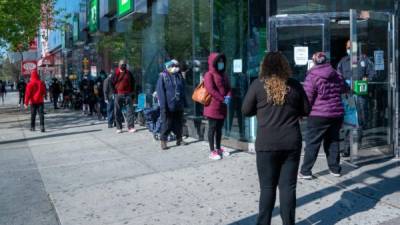 Personas se protegen con una mascarilla en Nueva York mientras mantienen la distancia en una fila. Foto: AFP