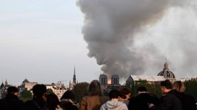 Personas observan que el humo se eleva a medida que la histórica Catedral de Notre-Dame se quema en el centro de París. AFP