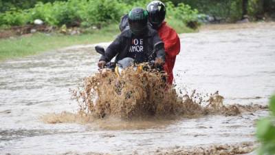 Dos hombres se transportan en motocicleta en una calle inundada por el desbordamiento del río Chamelecón hoy, en la ciudad de San Pedro Sula (Honduras).