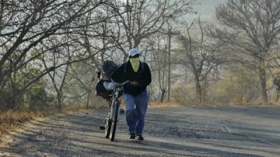 Un hondureño se traslada a pie en la carretera hacia el norte del país. Las temperaturas correspondientes a la temporada de verano en Honduras muestran árboles secos en zonas de altas temperaturas.