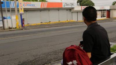 Un joven espera en una parada de bus frente a negocios cerrados por el estado de sitio.