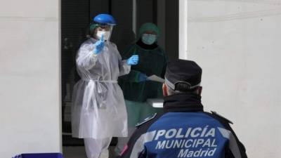 Una foto muestra a un trabajador de la salud haciendo un gesto a un oficial de policía municipal durante las pruebas de detección del coronavirus COVID-19 en Madrid. Foto AFP