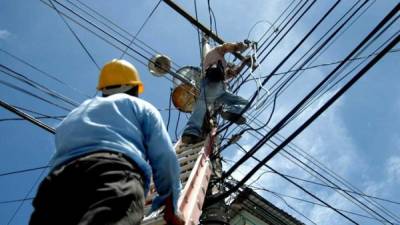 Dos empleados de la Enee realizan trabajos de mantenimiento en el cableado de un poste eléctrico.