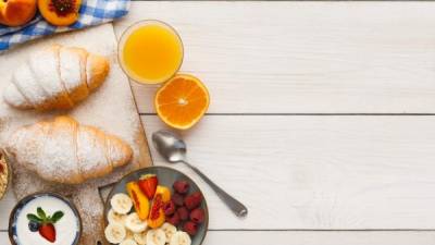 Traditional french breakfast menu background. Yogurt with fresh berries, glass of orange juice, fruit plate and croissants on wooden table, top view, copy space