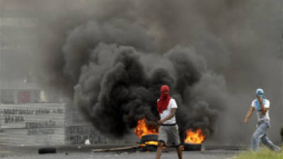 Masked demonstrators walk past a barricade set on fire during a protest in downtown Colon, Panama, Wednesday, Oct. 24, 2012. Panama's President Ricardo Martinelli said Wednesday that he is willing to cancel plans to sell state-owned land in a duty-free zone on the Panama Canal following a week of sometimes violent protests in which a 10-year-old boy and two adults died. (AP Photo/Arnulfo Franco)