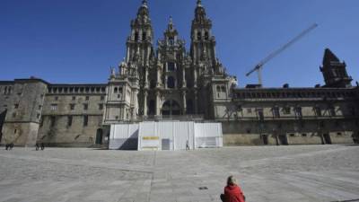 Una mujer se sienta afuera de la Catedral de Santiago de Compostela, en la plaza del Obradoiro, generalmente abarrotada, en Santiago de Compostela, pero hoy luce desolada.
