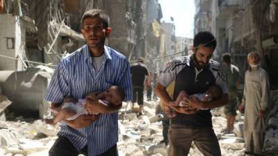 Dos hombres huyen con sus bebés tras un bombardeo en Alepo. AFP.