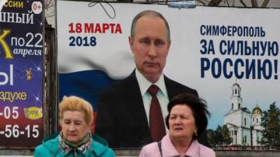 Dos mujeres caminan junto a un cartel de la campaña de Putin en Simferopol, Crimea.