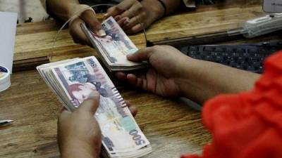 Una cajera entrega el cambio el billetes de moneda nacional a una mujer en un banco de La Ceiba.
