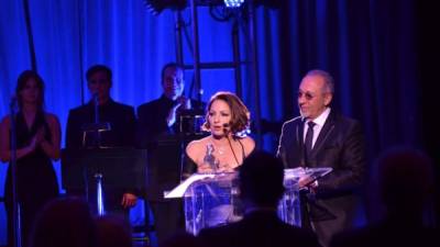 Emilio Estefan le entrega la estatuilla a Gloria Estefan, una escultura con forma de mujer tocando la guitarra.