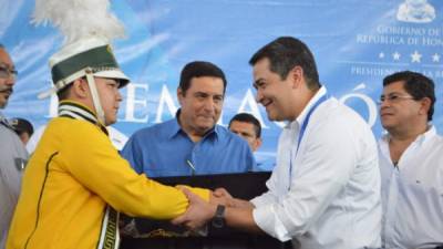 El presidente Hernández entrega un instrumento a un joven. Chedrani observa.