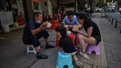 Una familia con máscaras faciales come junto a un puesto en Wuhan, en la provincia central de Hubei de China. Foto AFP